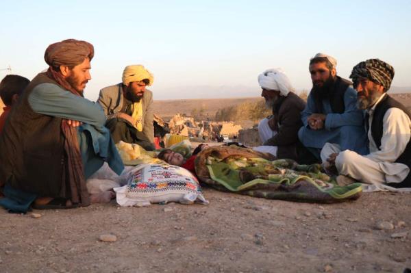 Afghan men sit near the bodies of those killed in the earthquakes that devastated the western part of the country on Saturday. Bodies of children are seen under blankets.
